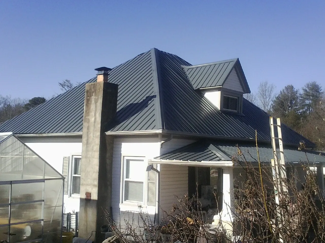 Dark blue standing seam metal roof on a white farmhouse with dormer — Slate & Tile Roof Repair by Roofing Brothers in Gladewater