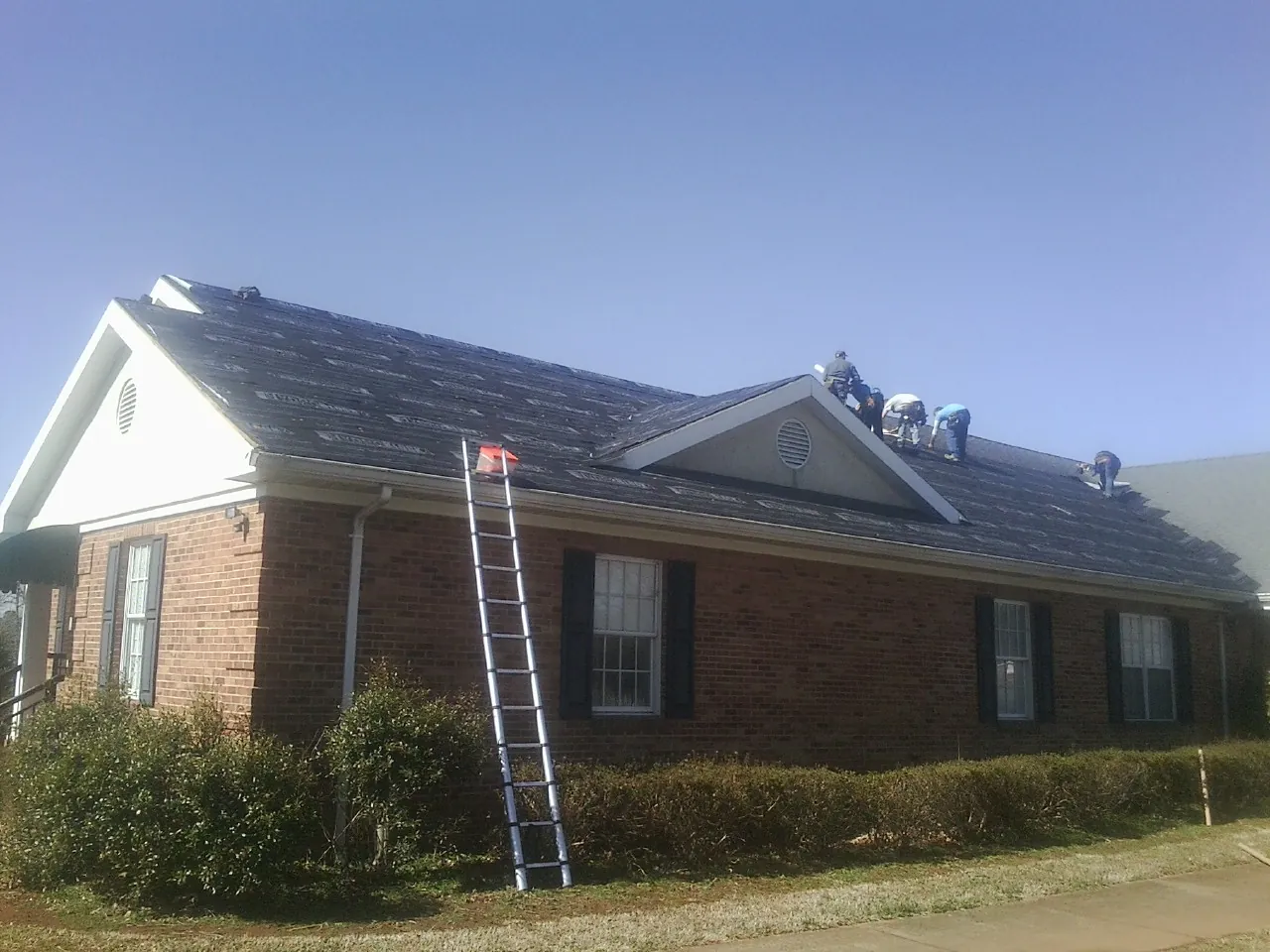 Crew tearing shingles off a brick ranch roof with a ladder set — Emergency Roof Repair work by our crew in Gladewater