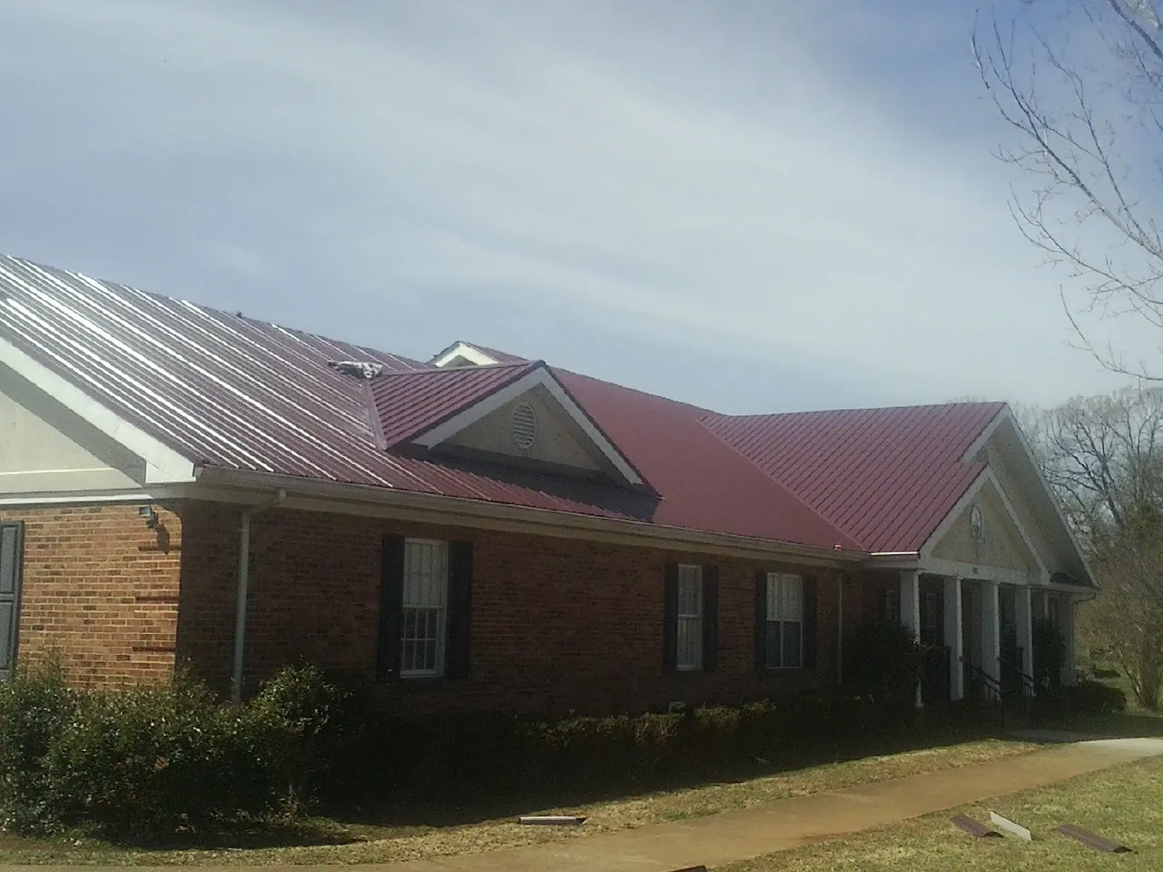 Red metal roof with gabled entries on a long brick building, from a Hail Damage Roof Repair job in Gladewater