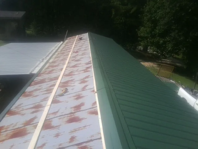 Old rusted panels beside newly installed green metal roofing — Wind Damage Roof Repair by Roofing Brothers in Gladewater