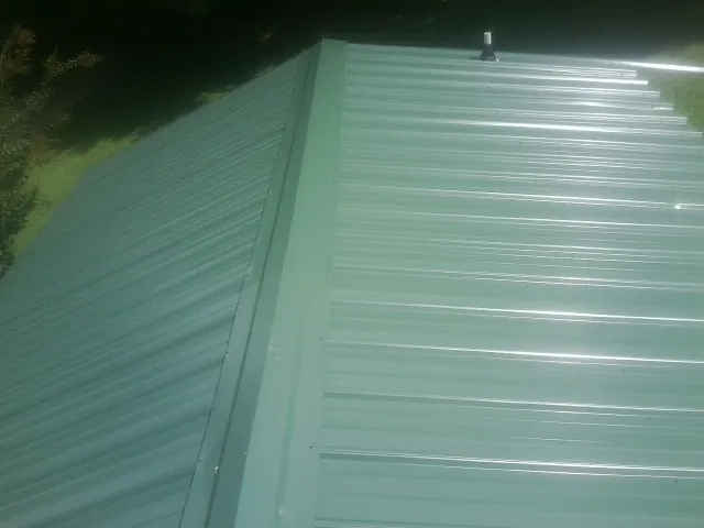 New green metal panels meeting at the ridge of a roof — Flat Roof Repair work by our crew in Gladewater