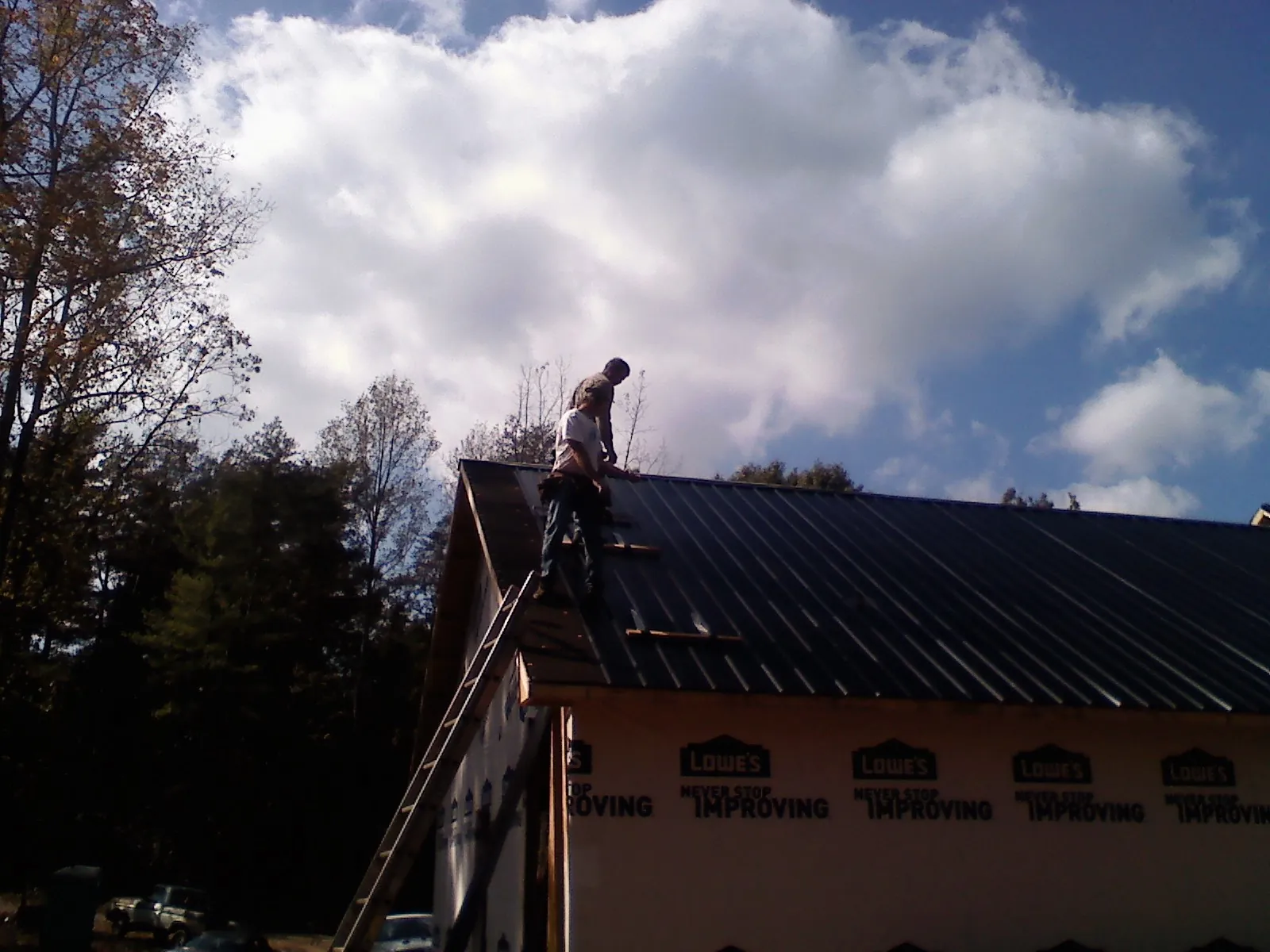 Roofer fastening dark metal panels high against a cloudy sky, from a Roof Inspection job in Gladewater