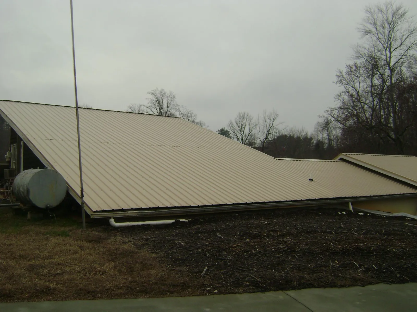 Wide tan metal roof plane seen from the ground beside a propane tank in Gladewater