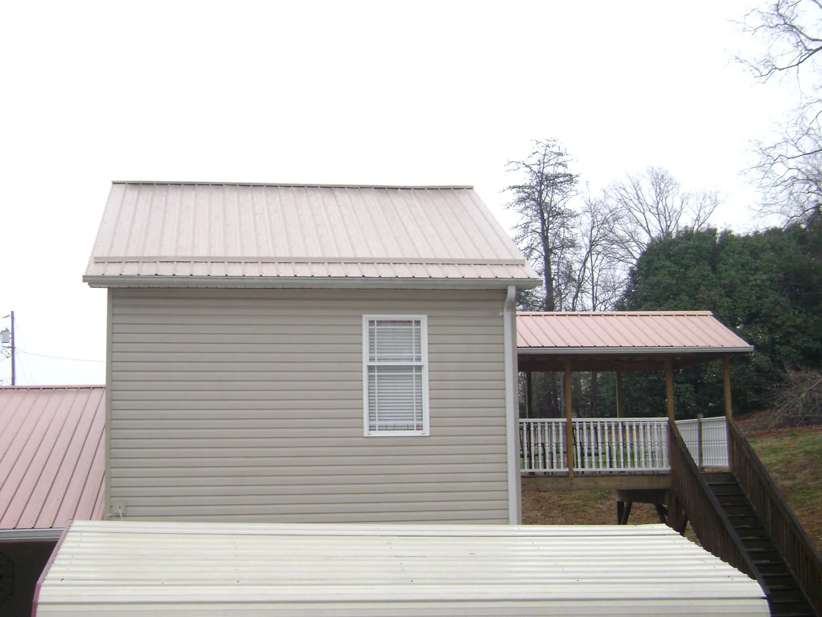 Tan metal roofs on a two story addition and attached porch, from a Roof Replacement job in Gladewater